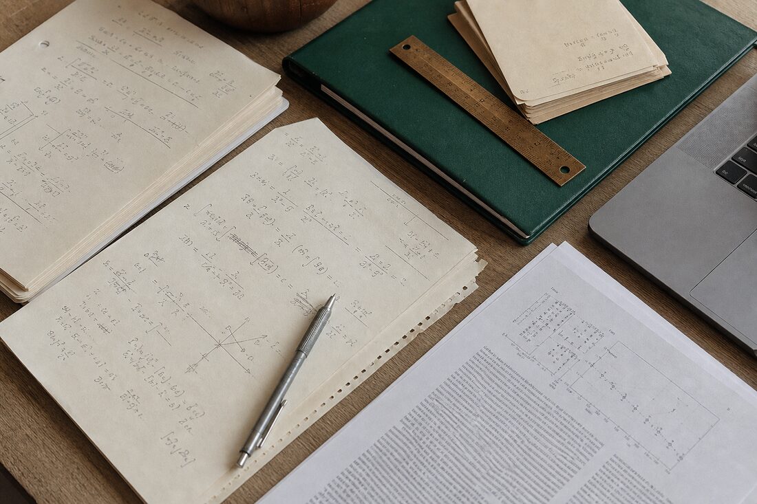 A researcher's desk with handwritten equations, a printed paper, and a bronze ruler
